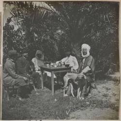 Voyage en Algérie : groupe d'hommes assis autour d'une table dans un jardin à Sidi-Okba (Henri Evenepoel) - Muzeo.com